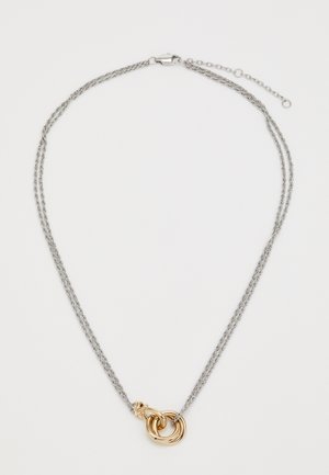 Sølv dobbeltkjede med en gull sammenvevd sirkulær vedheng og en justerbar lås på en hvit bakgrunn.