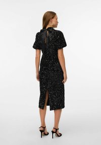 Melnā zamaka kleita ar īsām pūkām piedurknēm, garumu līdz pusmugurai un aizmugurējo šķēlumu. Piesieta sātīgā samta detaļa pie kakla pievieno eleganci.