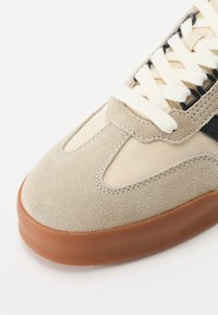 Beige Wildleder- und tanfarbene Gummisneaker mit cremefarbenen Schnürsenkeln; ausgestattet mit Mesh-Einsätzen, gestickten Akzenten und einem runden Zehendesign.