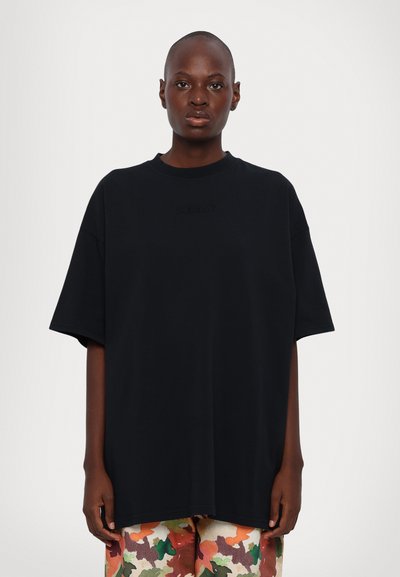 T-shirt en coton noir surdimensionné avec des manches courtes et un col ras du cou à côtes ; présente un logo en relief subtil sur la poitrine pour un détail.