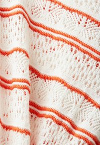 Tissu blanc tricoté avec des motifs ajourés, présentant des rayures horizontales alternées en orange vif et rouge.