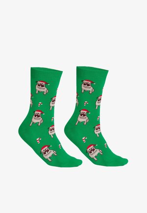 Grüne Socken mit wiederholten Mustern von Möpsen, die rote Weihnachtsmützen und Zuckerstangen tragen, aus weichem Textilmaterial gefertigt.