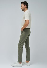 Camisa corta de manga beige claro, pantalones ajustados verde oliva y zapatillas blancas. La tela es suave, con un ajuste entallado y mínimo detalle.
