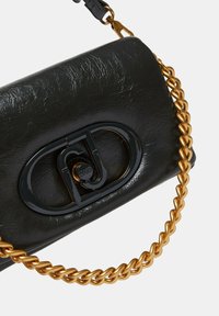 Bolso de mano de cuero negro texturizado con un cierre negro brillante y una correa de cadena gruesa en tono dorado. Forma rectangular compacta.
