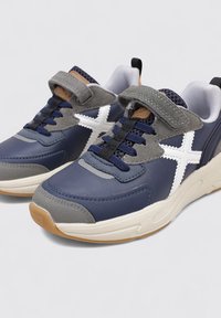 Sneakers blu navy con accenti grigi, design a stella bianca, linguetta in rete e cinturino in Velcro. Presentano suola in gomma e materiali testurizzati.