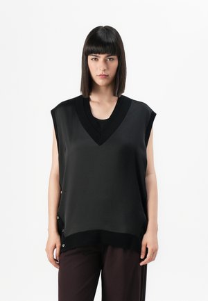 Top noir sans manches avec un décolleté en V, avec un tissu texturé et des accents de boutons sur les côtés, associé à un pantalon sombre, présenté sur un fond blanc.