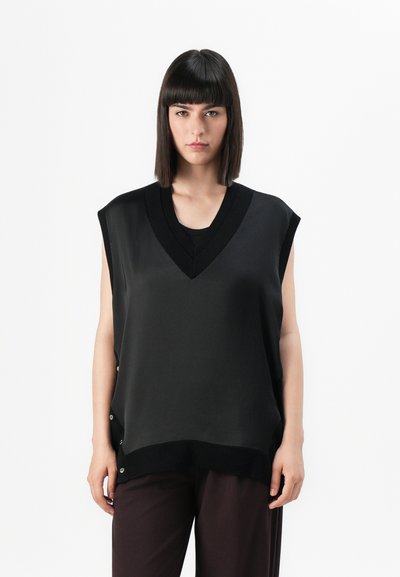 Top noir sans manches avec un décolleté en V, avec un tissu texturé et des accents de boutons sur les côtés, associé à un pantalon sombre, présenté sur un fond blanc.
