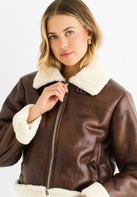 Brown faux leather jacket featuring a cream-colored, fluffy collar and cuffs, zip closure, and diagonal seam detailing.