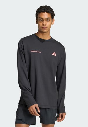Jeune homme portant un t-shirt noir à manches longues avec le texte et le logo "RUNNING STATE OF MIND", associé à un short de sport noir.