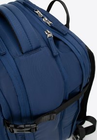 Marineblauwe rugzak met een gestructureerde stof, dubbele ritssluitingen, gevoerde schouderbanden en een verstelbare zijgesp.