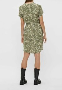 Grünes Blumenkleid mit kurzen Ärmeln, tailliert, knielang, aus leichtem Stoff. Kombiniert mit schwarzen klobigen Stiefeln.