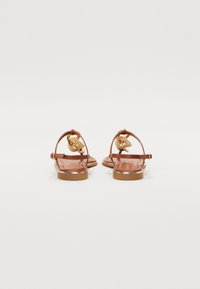 Sandalias de cuero marrón con una correa en la parte trasera, detalles en hardware dorado, suela plana y textura suave. Presenta un diseño sencillo con mínimas ornamentaciones.
