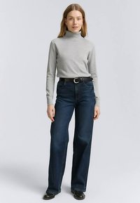 Šedý rolák spárovaný s tmavě modrými džínami s širokými nohavicemi. Černý opasek se stříbrnou přezkou. Modelka má na sobě černé kotníkové boty.