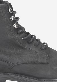 Bottine noire en cuir avec tige texturée, lacets plats, œillets en métal argenté et semelle en caoutchouc. Présente des coutures minimales et un bout arrondi.