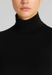 Maglione a collo alto nero realizzato in tessuto liscio e elastico, con una vestibilità aderente e colletto alto, senza motivi o decorazioni visibili.