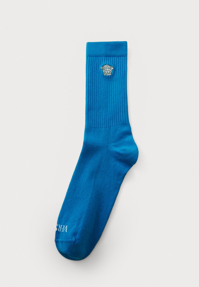 Blå sok lavet af ribbet stof med et dekorativt emblem på den øverste sektion. Har en glat tekstur og et forstærket tåområde.