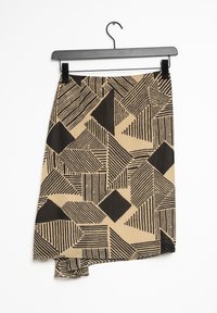 Asymmetrisk kjol gjord av lättviktsmaterial med ett abstrakt svart geometriskt mönster på en beige bakgrund. Hänger från en svart klämma.