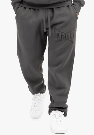 Gray, cotton blend joggers with a drawstring waist and a large, black TAPOUT logo on the left thigh, paired with white sneakers.