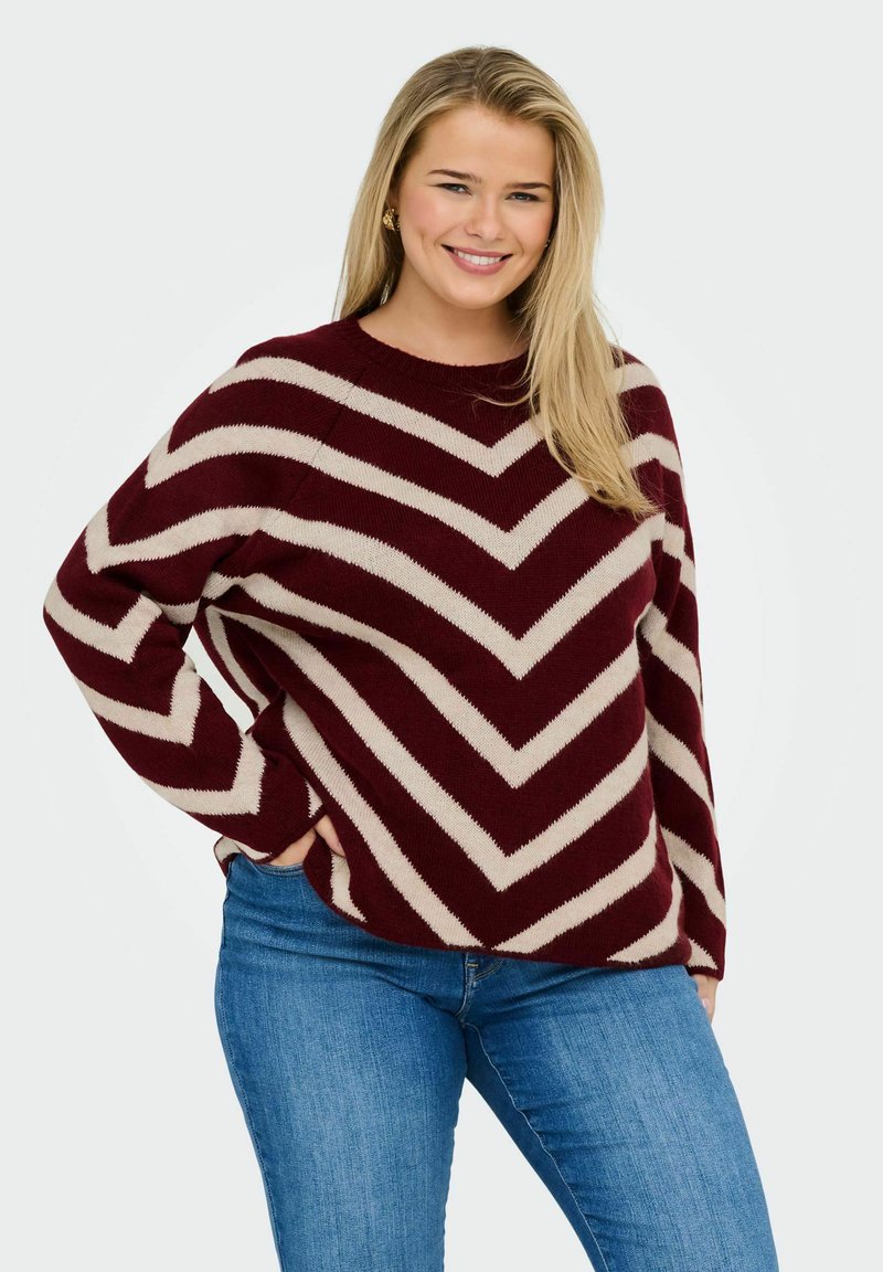 Maglione a righe bordeaux e crema con un motivo a zigzag, scollatura rotonda e vestibilità rilassata. Il materiale sembra morbido e sostenuto.