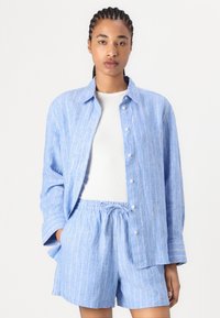 Chemise en lin bleu clair et shorts assortis avec des rayures verticales blanches. La chemise a un col à boutons et une coupe décontractée. Shorts avec ceinture élastique.