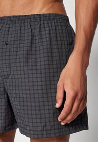 Black and gray checked swim shorts with an elastic waistband and a single button. Fabric appears lightweight with a soft texture.