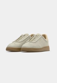 Light beige sneakers made of suede with a rubber sole, featuring a rounded toe, flat laces, and minimalistic design details.