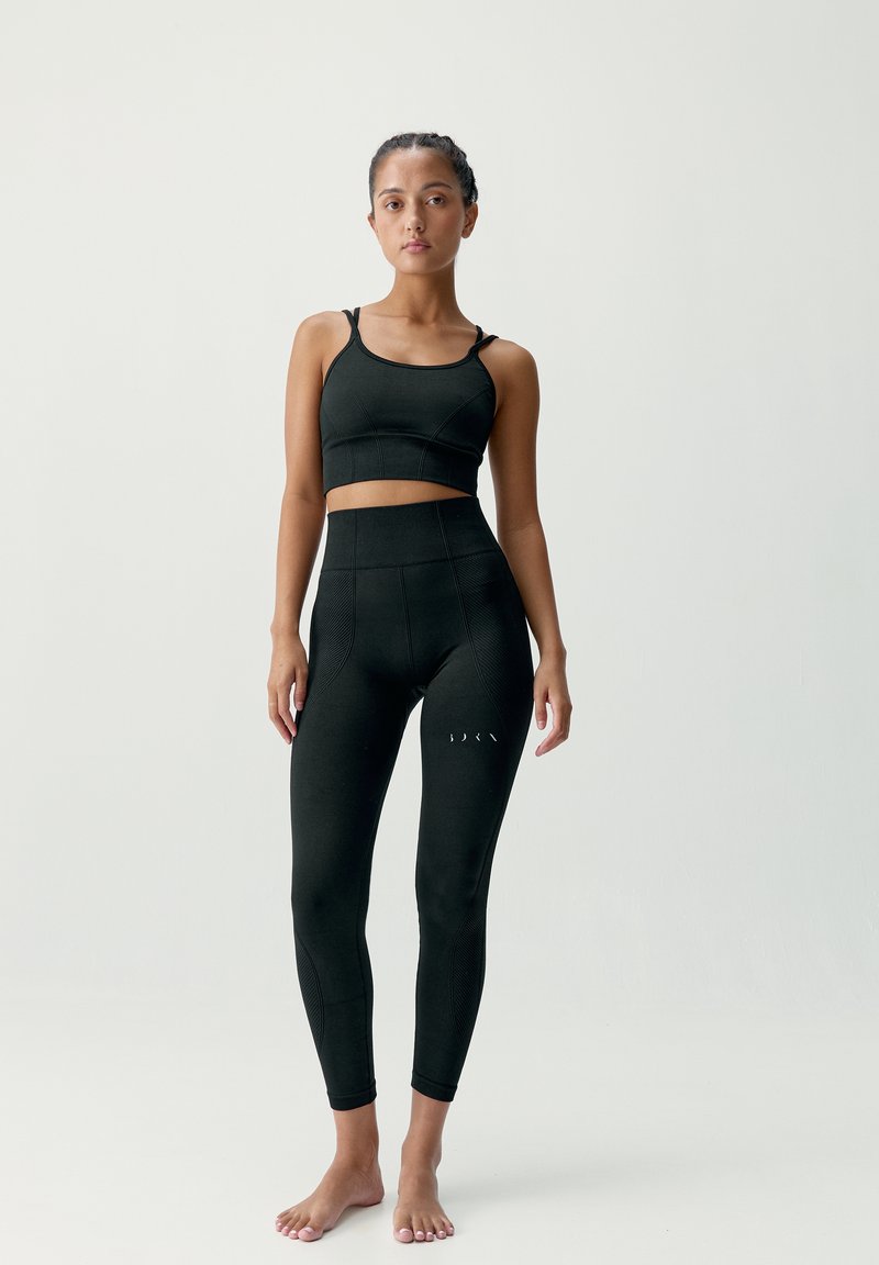 Czarny zestaw odzieży aktywnej, składający się z crop topu z cienkimi ramiączkami oraz legginsów z wysokim stanem, o gładkiej fakturze i subtelnych prążkowanych detalach.