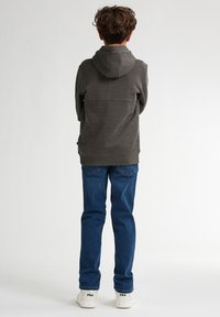 Felpa grigia scura con finitura texturizzata, dotata di cappuccio e orlo dritto, abbinata a jeans blu di denim e sneaker bianche.