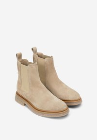 Bottes basses en daim beige avec panneaux latéraux élastiques, languettes de tirage et semelle texturée de couleur claire. Présentent un design élégant à embout arrondi.