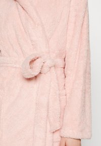 Pink fluffy robe featuring long sleeves, a tied waist, and a soft texture, ideal for comfort and warmth.