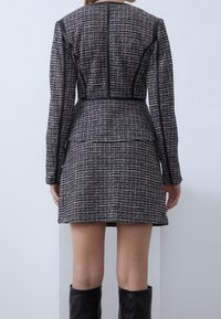 Přiléhavá krátká bunda z texturované černobílé tkaniny tweed s černými akcenty a dlouhými rukávy.