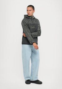 Hættetrøje i mørkegrå med en tekstureret mønster, med en sort panel og logo. Kombination med lyseblå brede jeans og sorte sko.