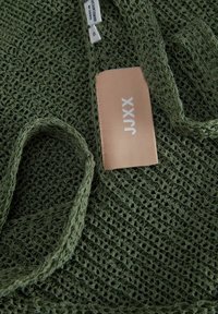 Tejido de punto verde con una trama abierta. Presenta una etiqueta de tela beige con "JXXX" impreso en blanco. Textura suave, diseño ligero.