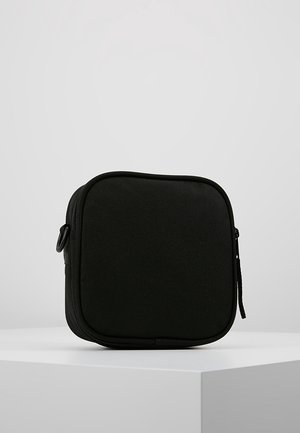 Schwarzes kompaktes quadratisches Reißverschluss-Etui aus Stoff, aufrecht stehend auf einer weißen Oberfläche vor einfachem hellem Hintergrund.