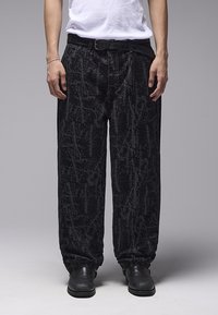 Μαύρο τζιν παντελόνι με υφή και αφηρημένο μοτίβο, σε χαλαρή γραμμή και με ελαστικές μανσέτες, σε συνδυασμό με μαύρα μποτάκια και λευκό πουκάμισο.