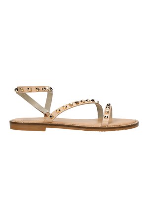 Sandali piatti color tan con un design minimalista. Presentano dettagli con borchie lungo le cinghie e il tallone, con una cinghia alla caviglia in suede beige chiaro.
