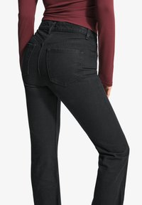 Črne denimske hlače s prilegajočo silhueto. Imajo visoko pasico, zasnovo s petimi žepi in minimalne šive. Gladka tekstura.