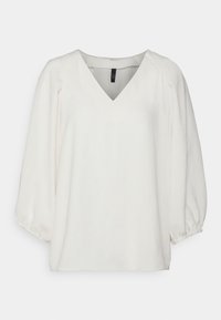 Blouse blanche à manches longues avec col en V et poignets froncés, présentée sur un fond clair uni.