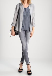 Šedá košile s dlouhým rukávem a knoflíky, na ní navy vzorovaný top, doplněná šedými skinny džíny a černými platformovými podpatky. Jednoduchá crossbody kabelka.