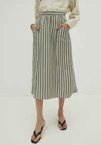 Gestreepte midi rok in zwart en wit, met een hoge taille, zijzakken en een vloeiende pasvorm. Materiaal lijkt lichtgewicht en soepel.