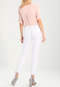 En rosa blus med korta ärmar och rynkad rygg, tillsammans med vita jeans med spetsdetaljer vid fållen. Silverfärgade högklackade skor bärs.
