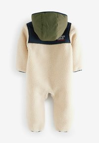 Combinaison en polaire crème, dotée d'une capuche verte et d'un panneau d'épaule bleu marine. Comprend une fermeture éclair et des poignets élastiques aux manches et aux jambes.