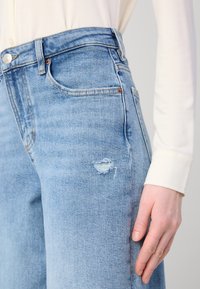 Lys blå denim jeans med avslappet passform, med et slitt hull på låret, fem lommer og sydd detaljer i sømmene.