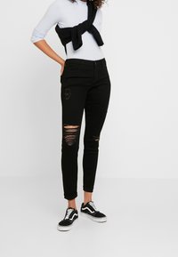 Svarta skinny jeans med slitna knän, hög midja och en mjuk textur. Matchas med vita snörskor och en ljus topp.