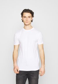 T-shirt blanc à manches courtes en coton doux, avec un col rond et une coupe légèrement ajustée, porté avec un jean foncé.