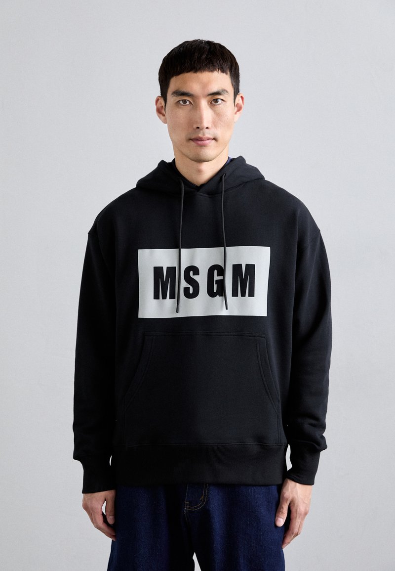 Schwarzer Hoodie mit einer vorderen Kängurutasche, der ein großes weißes Rechteck mit "MSGM" in fettem schwarzen Text zeigt. Weicher Stoff, lockere Passform.