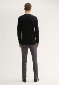 Black long-sleeve sweater with a ribbed texture, paired with gray trousers. Sweater features a rounded neckline and fitted cuffs.