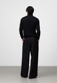 Czarny sweter z golfem w połączeniu z szerokimi czarnymi spodniami. Materiał wydaje się gładki, ma dopasowany krój i prążkowane mankiety.