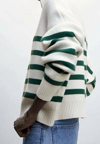 Cream sweater with green horizontal stripes, ribbed texture, dropped shoulders, and a loose fit, paired with light blue denim.