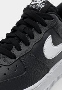 Nike Air Force 1 tenisice imaju gornjište od crne teksturirane kože, bijeli kožni swoosh i crne vezice s logotipom na jeziku.